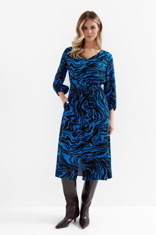 Na modelce sukienka o długości midi z rękawami o długości 7/8, dekoltem V, wiązana w talii  materiałowym paskiem, z rozcięciem u dołu eksponującym nogi