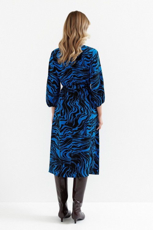 Na modelce stojącej tyłem sukienka o długości midi z rękawami o długości 7/8,  wiązana w talii  materiałowym paskiem, zapinana na plecach na kryty suwak