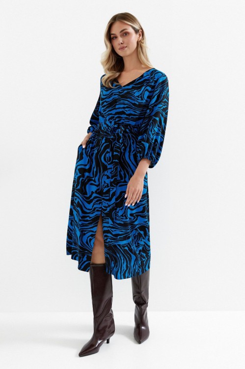 Na modelce sukienka o długości midi z rękawami o długości 7/8, dekoltem V, wiązana w talii  materiałowym paskiem, z rozcięciem u dołu eksponującym nogi