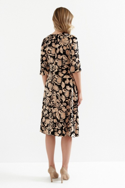 Na modelce stojącej tyłem sukienka w kolorze czarnym w brązowy roślinny wzór, o długości midi, lekko rozkloszowana, rękaw o długości 7/8 zakończony gumką, zapinana na kryty suwak