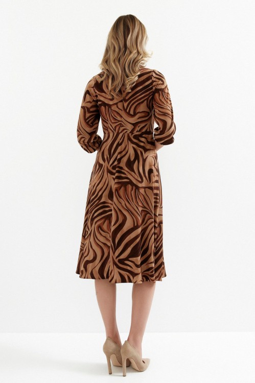 Na modelce stojącej tyłem sukienka w ciepłych odcieniach beżu i brązu, o długości midi, rozkloszowaną, z talią podkreśloną odcięciem oraz efektownym marszczeniem, z rękawami o długości 7/8 i okrągłym dekoltem