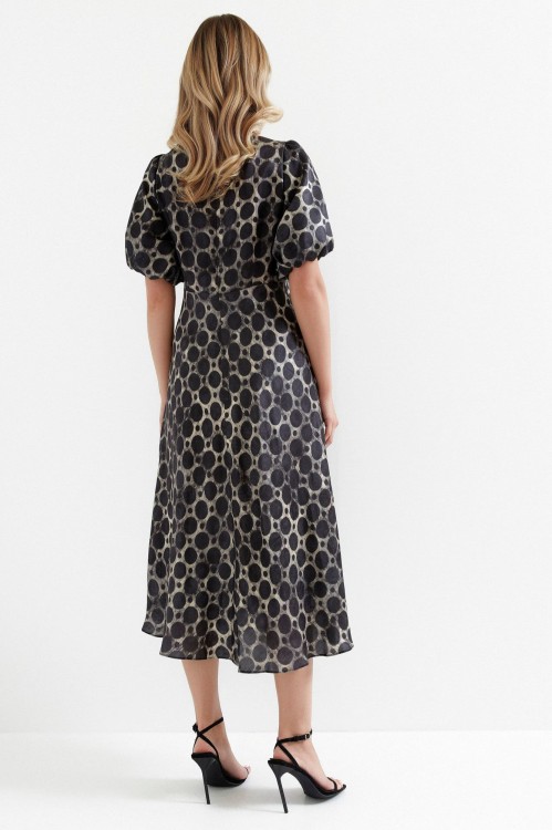 Na modelce sukienka o długości midi, w beżowy motyw roślinny na grafitowym tle, odcinana lekko powyżej talii, rozszerzana ku dołowi, z okrągłym dekoltem i krótkimi bufiastymi rękawkami