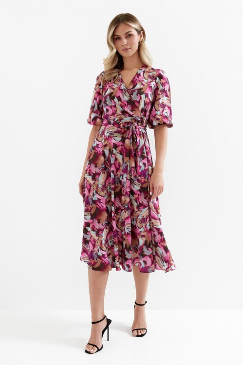 Na modelce sukienka rozkloszowana, kolorowa w odcieniach bordo, różu, brązu o długości midi z kopertowym dekoltem, wiązana w talii, rękaw do łokcia zakończony gumką