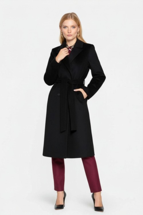 Na modelce stojącej przodem płaszcz w kolorze czarnym, z klasycznym kołnierzem, zapinany na guziki, dwurzędowy, przewiązany paskiem materiałowym, z wpuszczanymi kieszeniami o długości za kolano