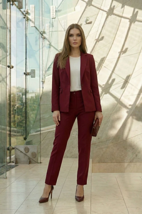 Na modelce stojącej przodem klasyczny żakiet w kolorze bordowym, z wyłogami, pionowymi zaszewkami modelującymi oraz kieszeniami z klapkami, zapinany na jeden guzik. Żakiet jest rozpięty