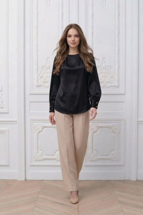 Na modelce stojącej przodem, czarna elegancka bluzka z długimi rękawami z mankietami zapinanymi na dwa guziki w kolorze złotym i niewielkim okrągłym dekoltem