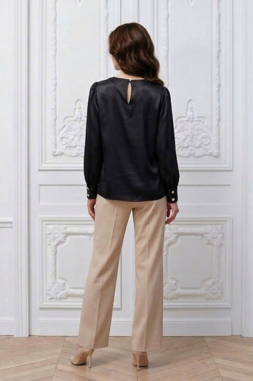 Na modelce stojącej tyłem, czarna elegancka bluzka z długimi rękawami z mankietami zapinanymi na dwa guziki w kolorze złotym, tyłu bluzki zapinany na guzik