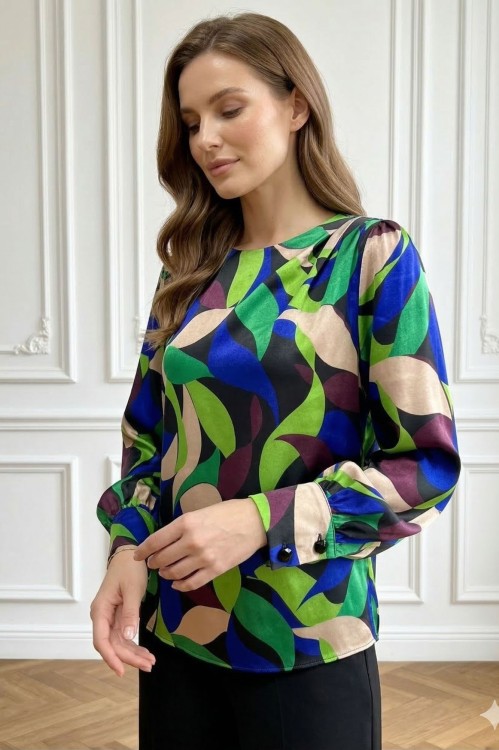 Na modelce stojącej przodem, elegancka, kolorowa bluzka z długim rękawem z mankietami; niewielkim, okrągłym dekoltem; ozdobnymi zakładkami na lewym ramieniu