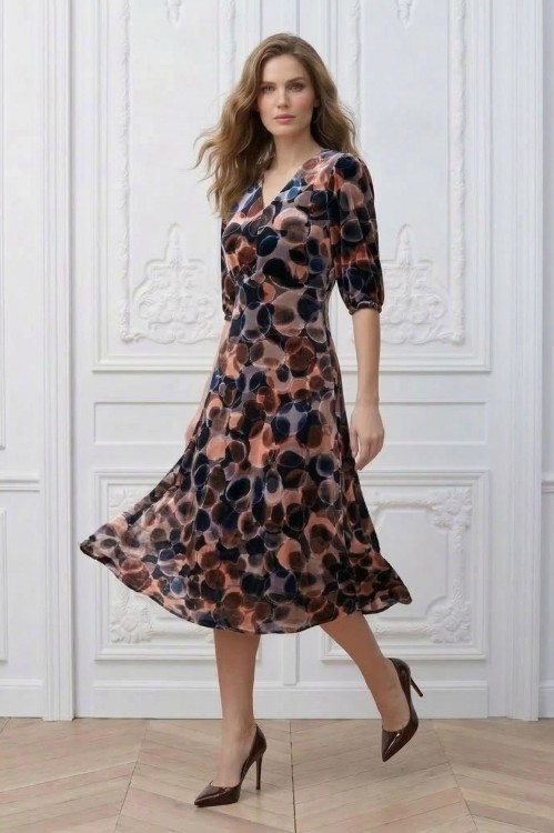 Na modelce stojącej przodem, sukienka w różnokolorowy wzór, o długości za kolana, lekko rozkloszowana, z odcięciem pod biustem w kształcie trójkąta, z lekkim przymarszczeniem, dekolt w literkę v, rękaw o długości 3/4 zakończony gumką.