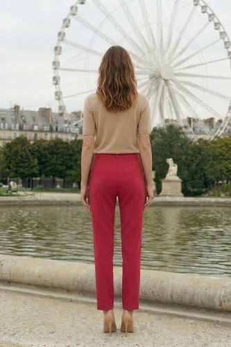 Na modelce stojącej tyłem klasyczne spodnie w kant, w kolorze malinowym, z wszywanym paskiem ze szlufkami i zaszewkami modelującymi