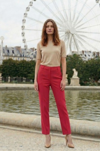 Na modelce stojącej przodem klasyczne spodnie w kant, w kolorze malinowym, zapinane z przodu na kryty suwak i haftkę, z wszywanym paskiem ze szlufkami oraz imitacją kieszonek