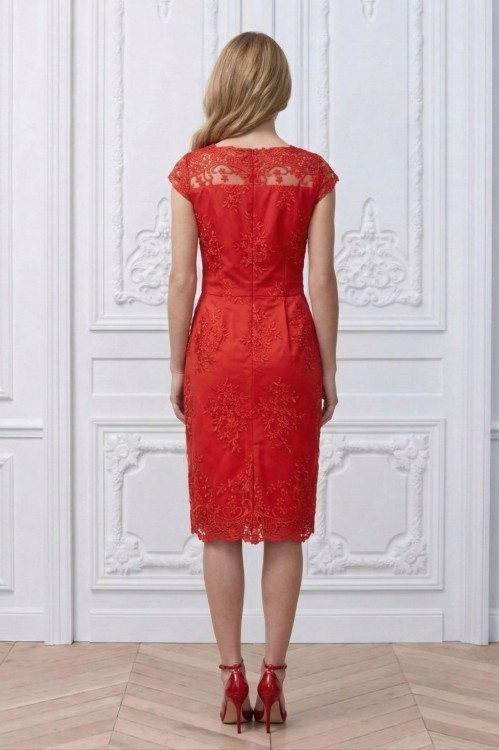 Na modelce stojącej tyłem czerwona sukienka z koronki, o długości za kolana, transparentny koronkowy karczek z łódkowym dekoltem podkreśla linię ramion. Poniżej odcięcia w talii z tyłu znajdują się cztery zaszewki , zapinana na kryty suwak