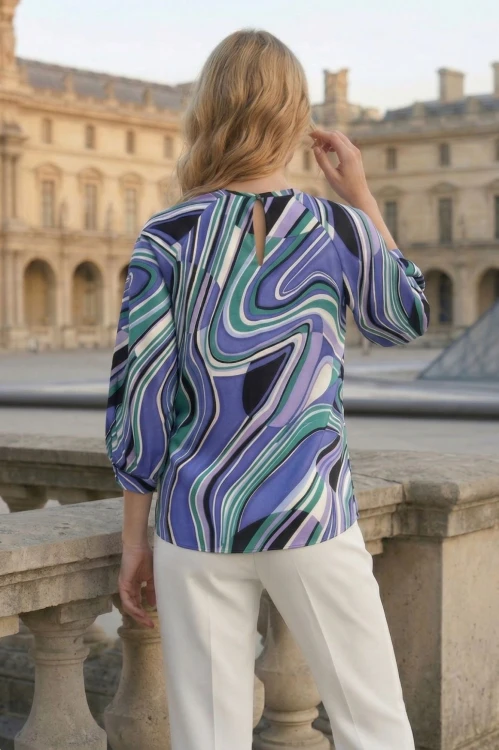 Na modelce stojącej tyłem bluzka o prostym fasonie w kolorowy abstrakcyjny wzór, niebiesko, zielono, fioletowy , z rękawami 3/4 z mankietami , zapinana na guzik