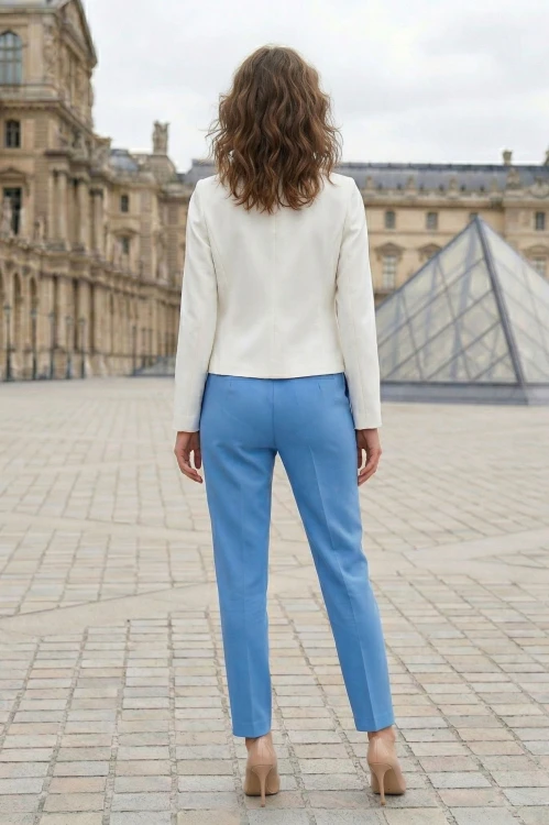 Na modelce stojącej tyłem krótki, dopasowany żakiet w kolorze białym.