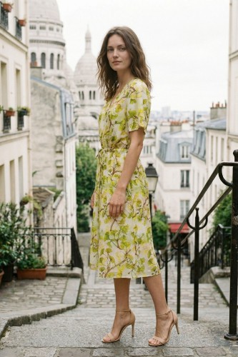 Na modelce stojącej lekko bokiem, sukienka midi, z lekko poszerzanym, krótkim rękawem, dekolt w kształcie V,  w pasie znajduje się pasek w tunelu, dół sukienki jest rozkloszowany, a w bocznych szwach znajdują się  kieszenie.