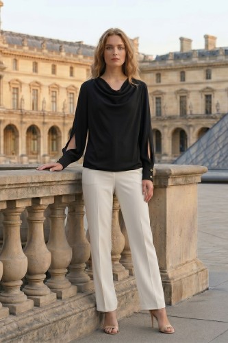 Na modelce stojącej przodem Elegancka czarna bluzka z dekoltem typu woda, długimi rękawami zakończonymi mankietami zapinanymi na dwa ozdobne guziki, powyżej mankietów efektowne rozcięcia