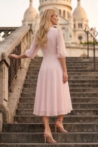 Na modelce stojącej tyłem sukienka midi w kolorze pudrowego różu, dół zwiewny rozkloszowany, rękawy 3/4 zakończone delikatną gumką