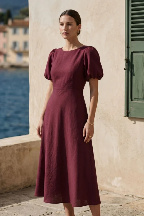 Na modelce sukienka o długości midi  rozkloszowana w odcieniach koloru bordowego, z okrągły dekoltem, odcięciem po wyżej talii, krótkim rękawkiem zakończonym gumką, tworzącą bufkę.