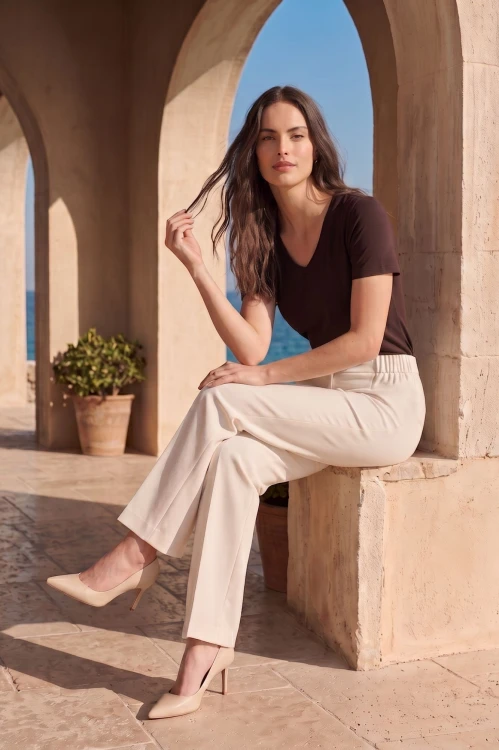 Na modelce eleganckie, letnie spodnie w kant, w kolorze śmietankowej bieli. Jest to model o szerokiej nogawce z zaprasowanymi kantami. Po bokach spodni wszyta w pasek guma. Spodnie posiadają kieszenie