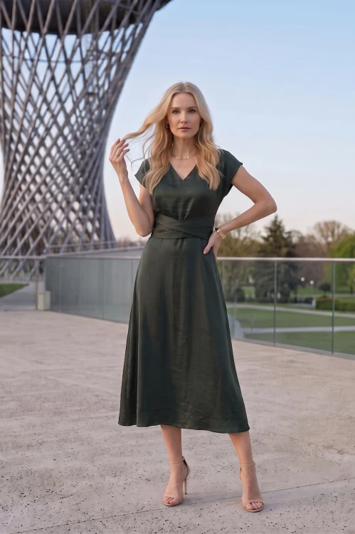 Na modelce midi sukienka w kolorze butelkowej zieleni, dekolt w delikatny serek, rękaw krótki reglanowy, w pasie materiałowa ozdoba, dół sukienki lekko rozkloszowany