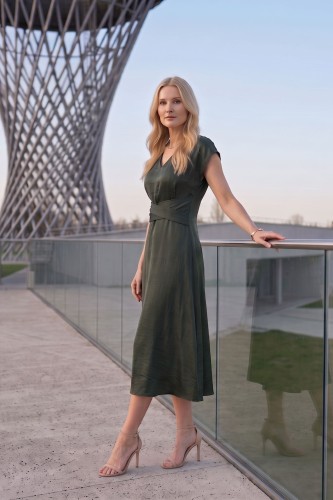 Na modelce midi sukienka w kolorze butelkowej zieleni, dekolt w delikatny serek, rękaw krótki reglanowy, w pasie materiałowa ozdoba, dół sukienki lekko rozkloszowany