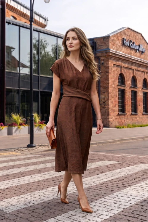Na modelce midi sukienka w kolorze mlecznej czekolady, dekolt w delikatny serek, rękaw krótki reglanowy, w pasie materiałowa ozdoba, dół sukienki lekko rozkloszowany