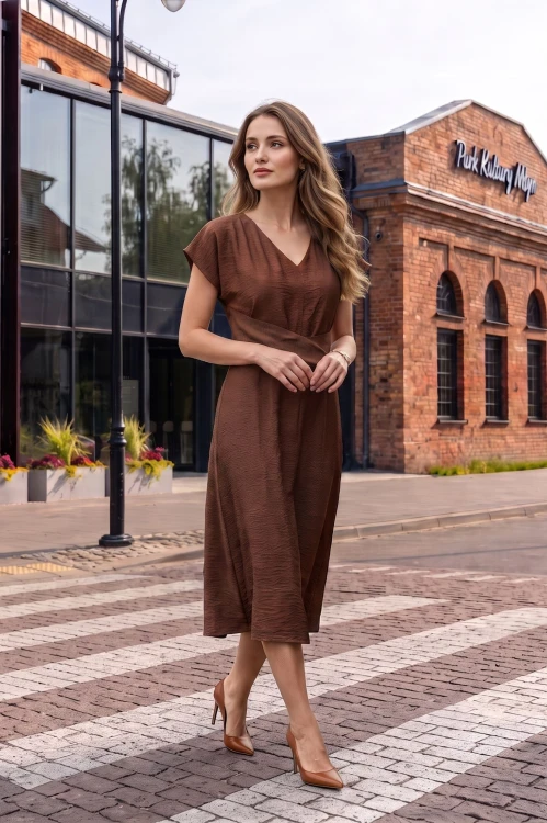 Na modelce midi sukienka w kolorze mlecznej czekolady, dekolt w delikatny serek, rękaw krótki reglanowy, w pasie materiałowa ozdoba, dół sukienki lekko rozkloszowany
