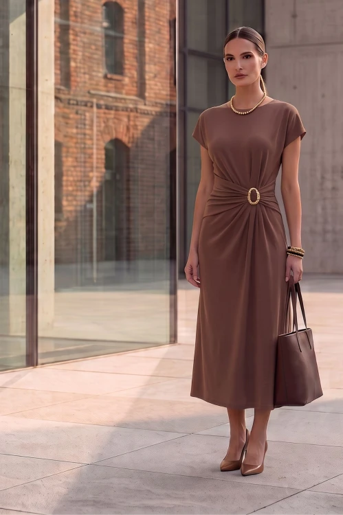 Na modelce midi sukienka w kolorze czekoladowym, dekolt w delikatny okrągły, rękaw krótki reglanowy, w pasie materiałowa ozdoba z biżuteryjnym akcentem, dół sukienki lekko rozkloszowany