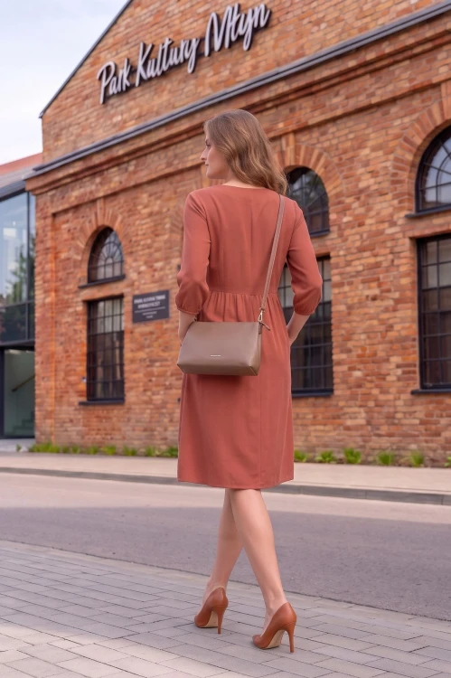Na modelce widocznej z tyłu, sukienka w kolorze herbacianym, o długości do kolan, z odcięciem lekko powyżej talii oraz krytym suwakiem na plecach, rękawy 3/4