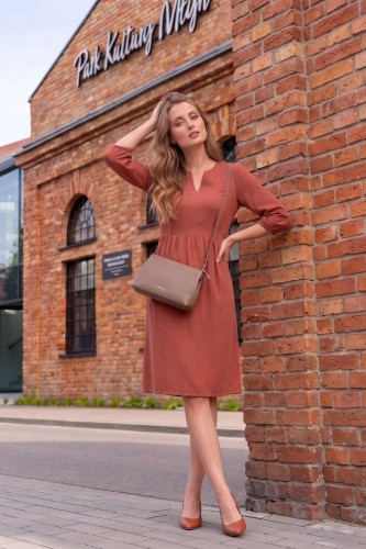 Na modelce stojącej przodem, sukienka w kolorze herbacianym, o długości do kolan. Sukienka ma odcięcie lekko powyżej talii, dekolt w v oraz wszywane rękawy długości 3/4
