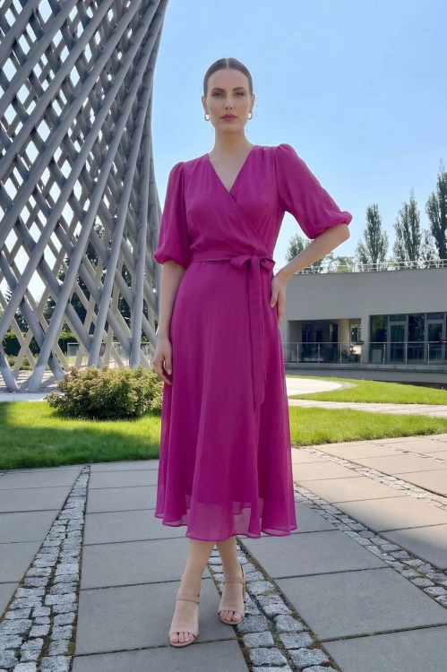 Na modelce stojącej przodem sukienka kolorze fuksji, o długości midi, rozkloszowana, z kopertowym dekoltem, 3/4 rękawami i materiałowym paskiem w talii