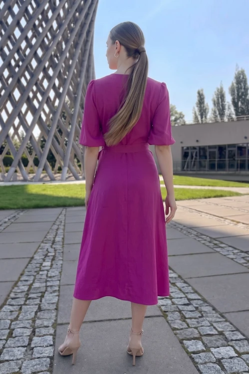 Na modelce stojącej tyłem sukienka w kolorze fuksji, o długości midi, rozkloszowana, 3/4 rękawami i materiałowym paskiem w talii, zapinana na plecach na kryty suwak