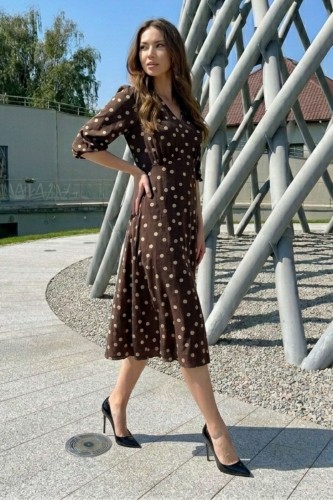 Na modelce sukienka w kolorze czekoladowym w beżowe groszki, o długości midi, lekko rozkloszowana, z odcięciem pod biustem w kształcie trójkąta, z lekkim przymarszczeniem, dekolt w literkę v, rękaw o długości 7/8 zakończony gumką.