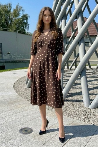 Na modelce sukienka w kolorze czekoladowym w beżowe groszki, o długości midi, lekko rozkloszowana, z odcięciem pod biustem w kształcie trójkąta, z lekkim przymarszczeniem, dekolt w literkę v, rękaw o długości 7/8 zakończony gumką.
