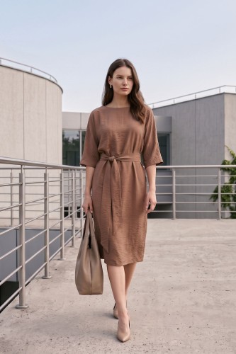 Na modelce stojącej przodem, sukienka w kolorze mlecznej czekolady, talia podkreślona paskiem, niewielki okrągły dekolt, rękawek kimonowy o długości za łokieć, dół sukienki za kolana lekko rozkloszowany
