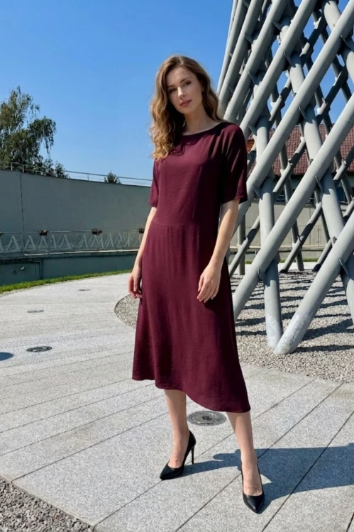 Na modelce stojącej przodem, sukienka midi w kolorze bordowym, z obniżoną talią, niewielki okrągły dekolt, rękawek kimonowy o długości do łokcia, dół sukienki  rozkloszowany