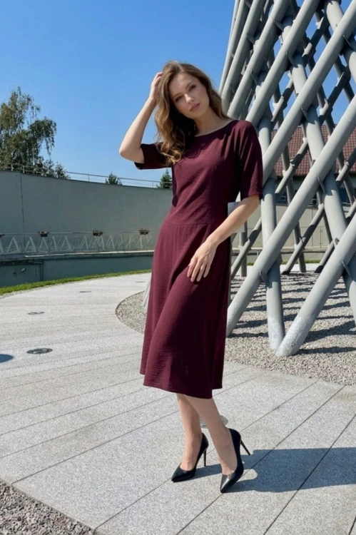 Na modelce stojącej przodem, sukienka midi w kolorze bordowym, z obniżoną talią, niewielki okrągły dekolt, rękawek kimonowy o długości do łokcia, dół sukienki  rozkloszowany
