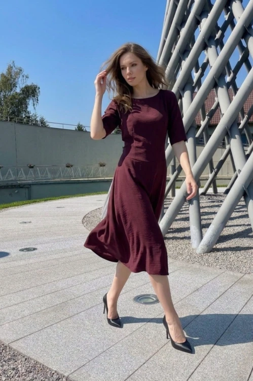 Na modelce stojącej przodem, sukienka midi w kolorze bordowym, z obniżoną talią, niewielki okrągły dekolt, rękawek kimonowy o długości do łokcia, dół sukienki  rozkloszowany