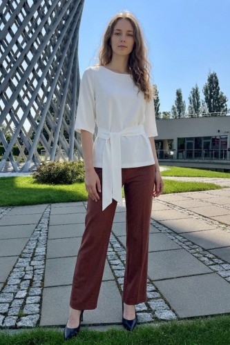 Na modelce biała bluzka z paskiem materiałowym, w tym samym kolorze co bluzka, z rękawami o długości 3/4, i niewielkim okrągłym dekoltem