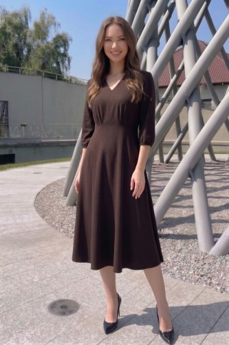 Na modelce, sukienka w kolorze ciemnobrązowym, o długości za kolana, lekko rozkloszowana, z odcięciem pod biustem w kształcie trójkąta, z lekkim przymarszczeniem, dekolt w literkę v, rękaw o długości 3/4 zakończony gumką.
