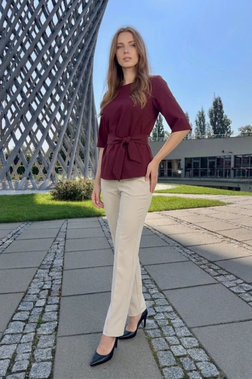 Na modelce bordowa bluzka z paskiem materiałowym, w tym samym kolorze co bluzka, z rękawami o długości 3/4, i niewielkim okrągłym dekoltem