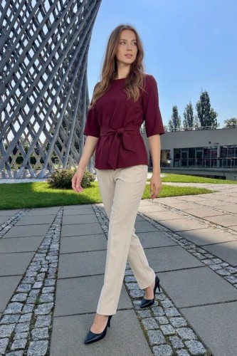 Na modelce bordowa bluzka z paskiem materiałowym, w tym samym kolorze co bluzka, z rękawami o długości 3/4, i niewielkim okrągłym dekoltem
