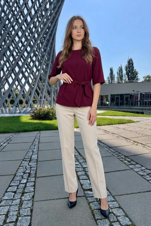 Na modelce bordowa bluzka z paskiem materiałowym, w tym samym kolorze co bluzka, z rękawami o długości 3/4, i niewielkim okrągłym dekoltem
