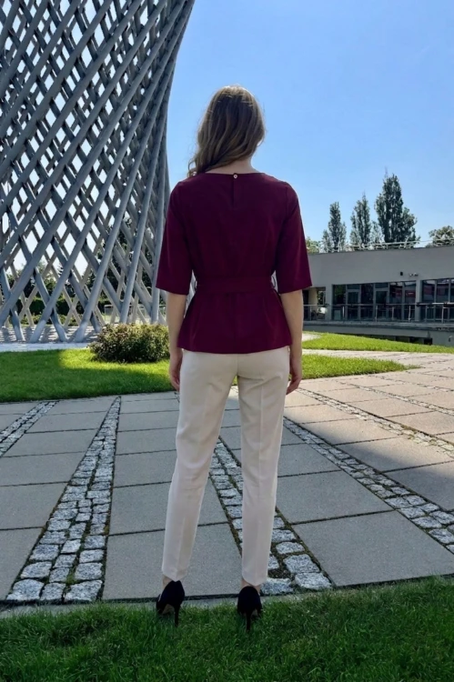 Na modelce stojącej tyłem bordowa bluzka z paskiem materiałowym, w tym samym kolorze co bluzka, z rękawami o długości 3/4, i niewielkim okrągłym dekoltem, na karku kryte pęknięcie zapinane na guzik