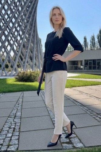 Na modelce czarna bluzka z paskiem materiałowym, w tym samym kolorze co bluzka, z rękawami o długości 3/4, i niewielkim okrągłym dekoltem