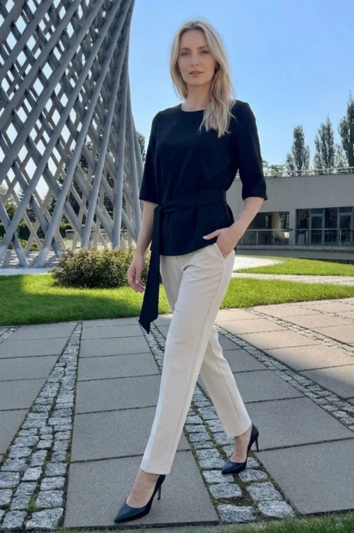 Na modelce czarna bluzka z paskiem materiałowym, w tym samym kolorze co bluzka, z rękawami o długości 3/4, i niewielkim okrągłym dekoltem