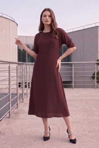 Na modelce stojącej przodem, sukienka midi w kolorze brązowym, z obniżoną talią, niewielki okrągły dekolt, rękawek kimonowy o długości do łokcia, dół sukienki  rozkloszowany