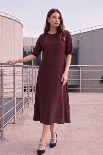 Na modelce stojącej przodem, sukienka midi w kolorze brązowym, z obniżoną talią, niewielki okrągły dekolt, rękawek kimonowy o długości do łokcia, dół sukienki  rozkloszowany