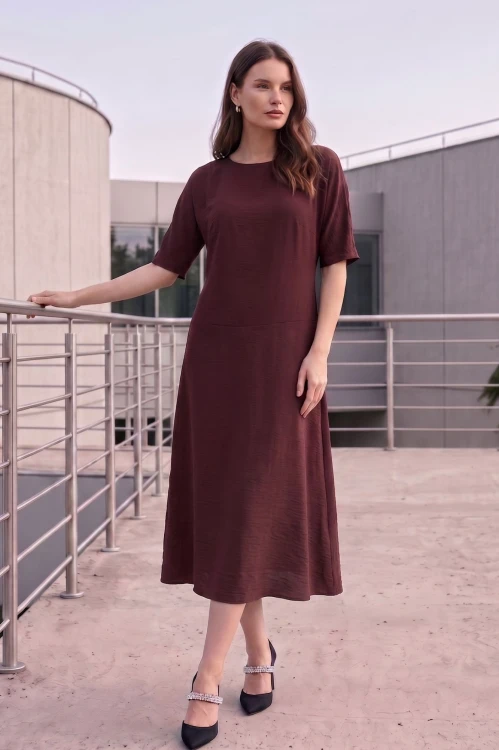 Na modelce stojącej przodem, sukienka midi w kolorze brązowym, z obniżoną talią, niewielki okrągły dekolt, rękawek kimonowy o długości do łokcia, dół sukienki  rozkloszowany