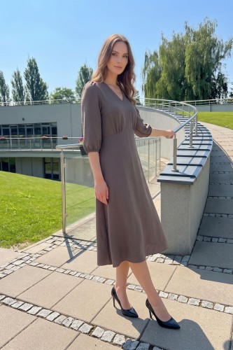 Na modelce, sukienka w kolorze fango, odcień brązu, o długości za kolana, lekko rozkloszowana, z odcięciem pod biustem w kształcie trójkąta, z lekkim przymarszczeniem, dekolt w literkę v, rękaw o długości 3/4 zakończony gumką.